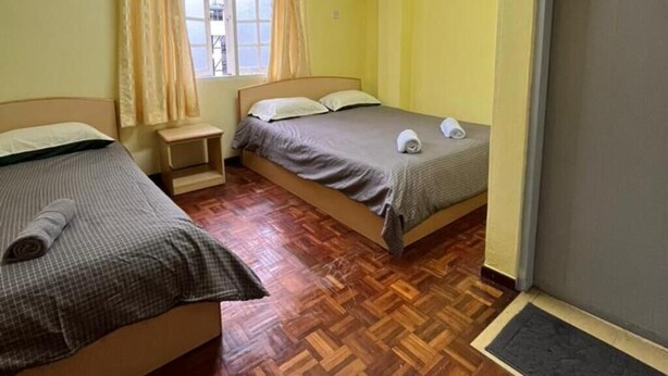 A small, compact room with two single beds, a window with curtains, and a wooden parquet floor. - Bderiah Cameron Guest House +Wi-Fi-Netflix-Garden view (Tanah Rata)