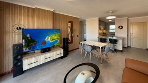 Egy modern nappali, amelyben síkképernyős televízió, étkező és konyha található.