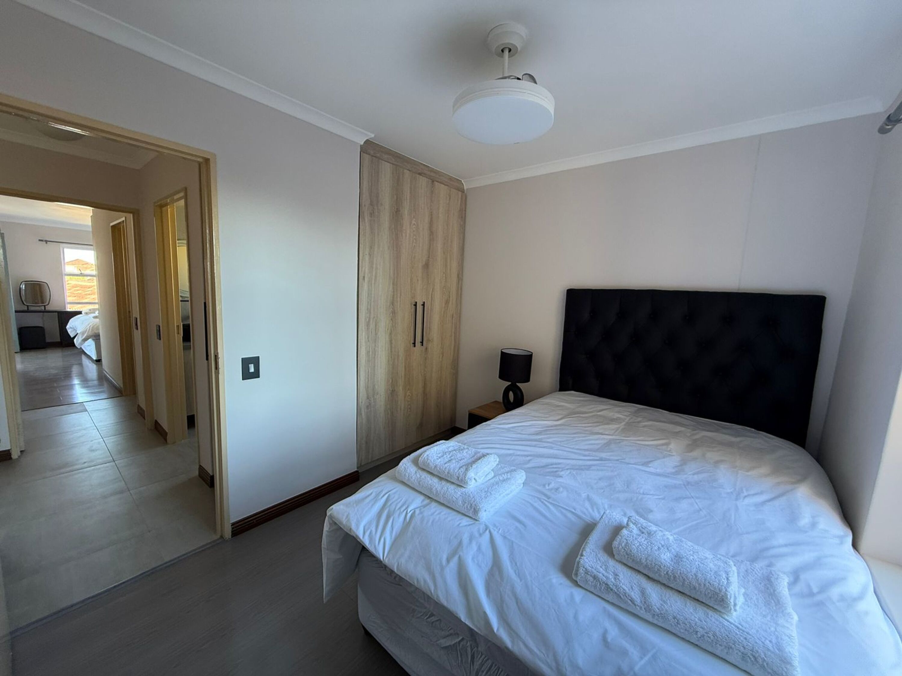 Een moderne hotelkamer met een groot bed, een kledingkast, een nachtkastje met een lamp en een plafondventilator.