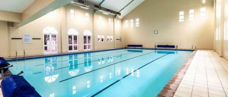 An indoor swimming pool with clear lanes, a tiled floor, and arched windows.