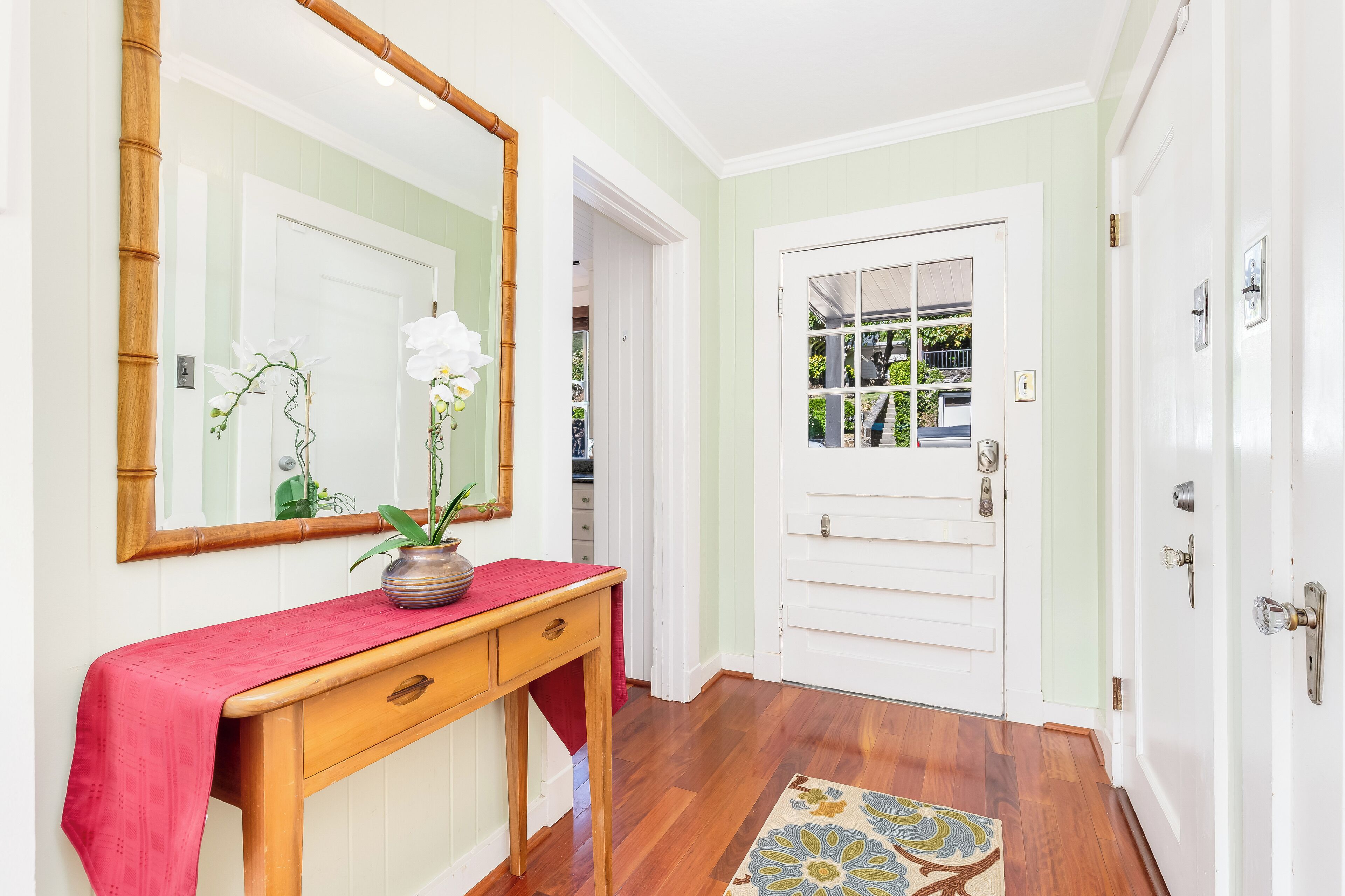 A hallway with a wooden console table, a mirror, and a potted orchid.