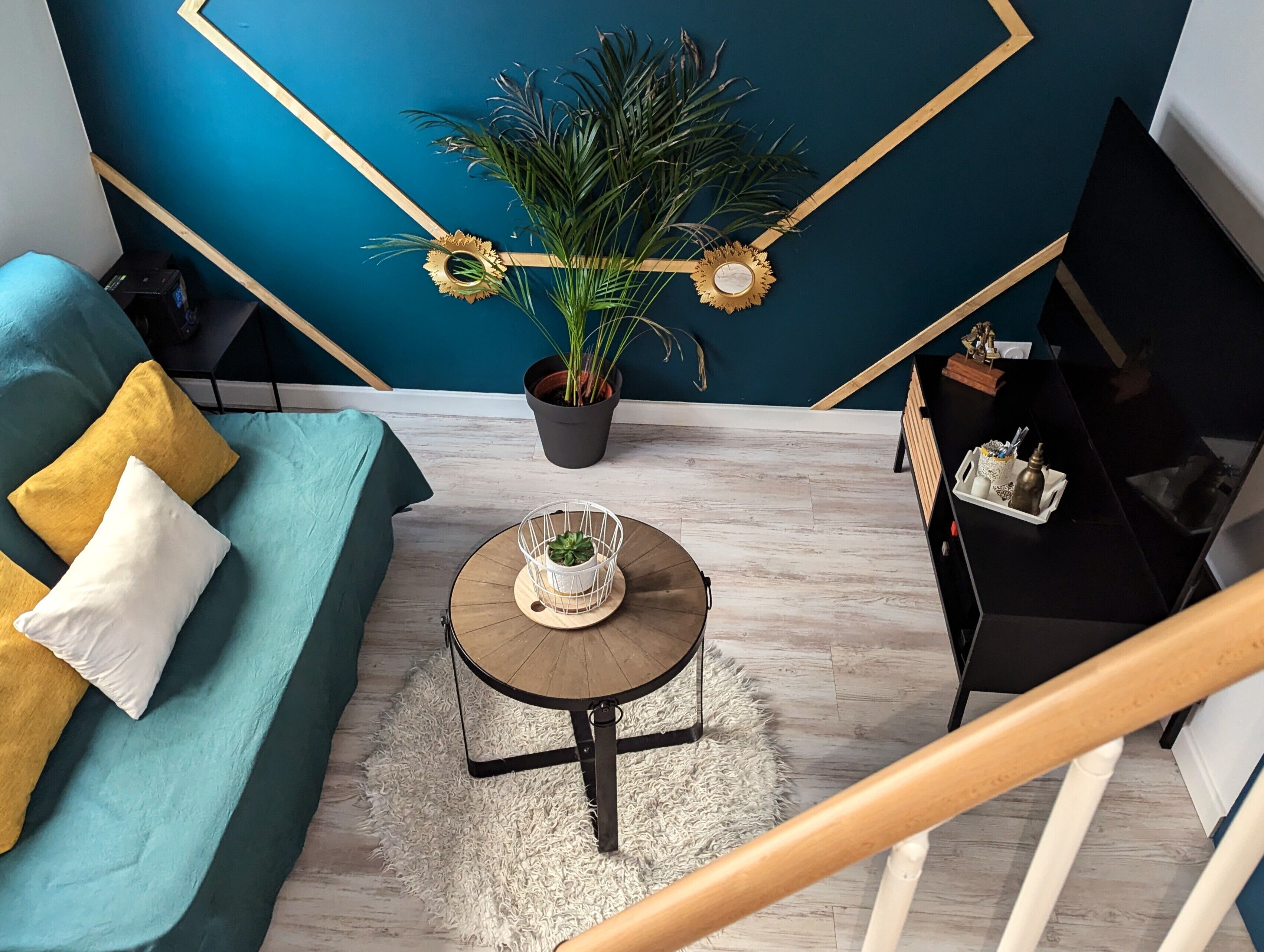 Een moderne woonkamer met een blauwgroene bank, een bijzettafeltje en een potplant.