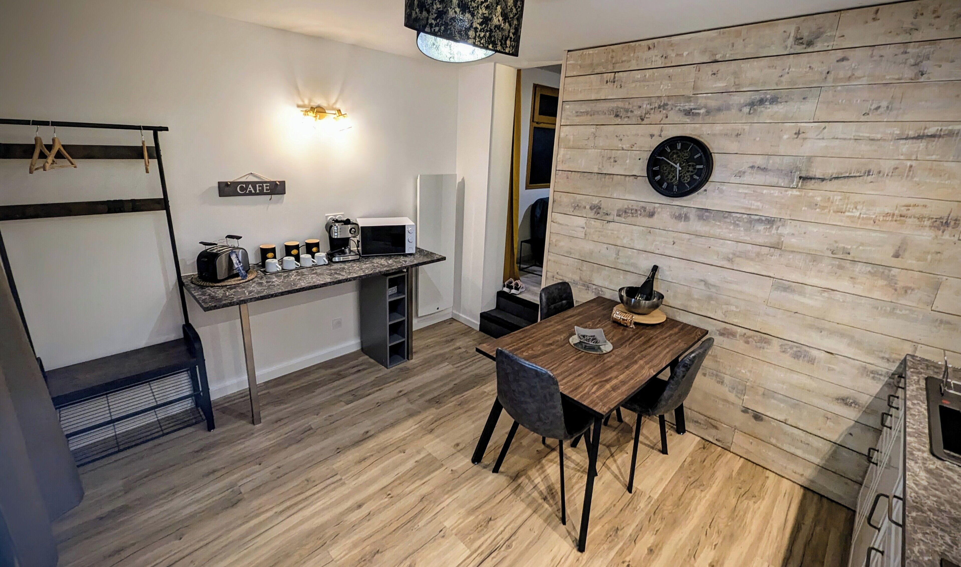 Een compacte keuken met een eethoek, een koffieapparaat en een klok aan de muur.