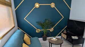 Una sala de estar moderna con un sofá verde azulado, una pequeña mesa redonda, una planta en maceta y un mueble para televisor.