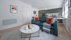 A modern living room with a green sofa, a round coffee table, and a kitchen in the background. - Modern 1BR near Tower Bridge and Tower of London (London)