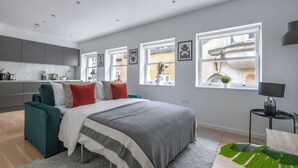 A modern bedroom with a large bed, a green sofa, and a small desk with a lamp. - Modern 1BR near Tower Bridge and Tower of London (London)