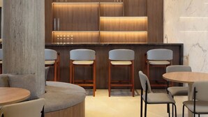 Un espace bar moderne avec des étagères en bois et un mur vert, entouré de sièges et doté d’un sol en marbre.