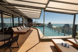 A rooftop pool area with lounge chairs and a view of the city. - Luxury Stay Steps from Praia Brava (Itajaí)