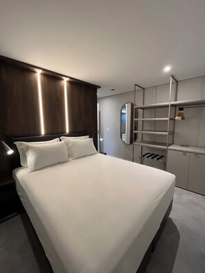 Ein modernes Hotelzimmer mit einem großen Bett, einem Nachttisch, einem Spiegel und integrierten Regalen.