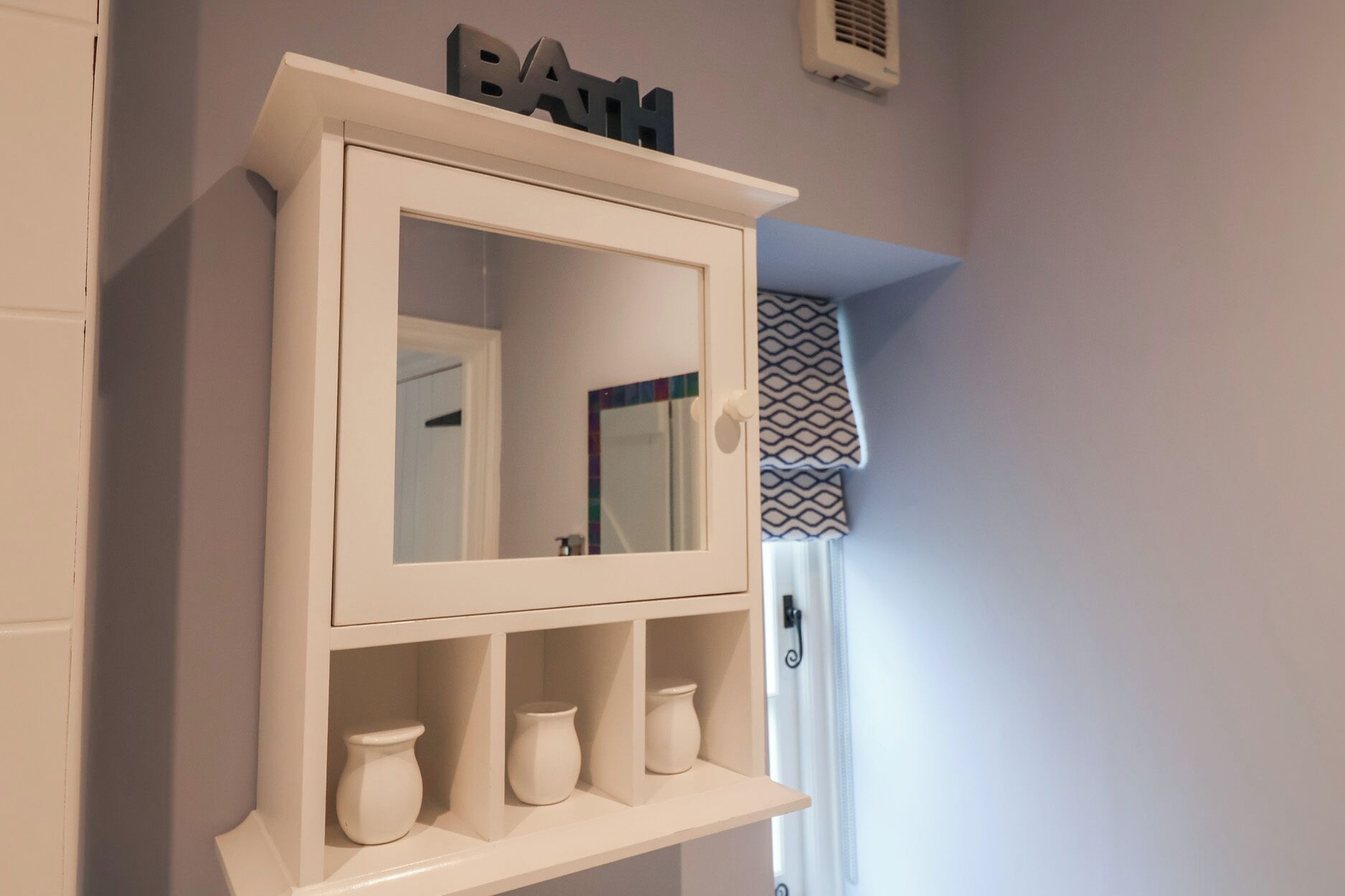 A white cabinet with a mirror and three vases on shelves.