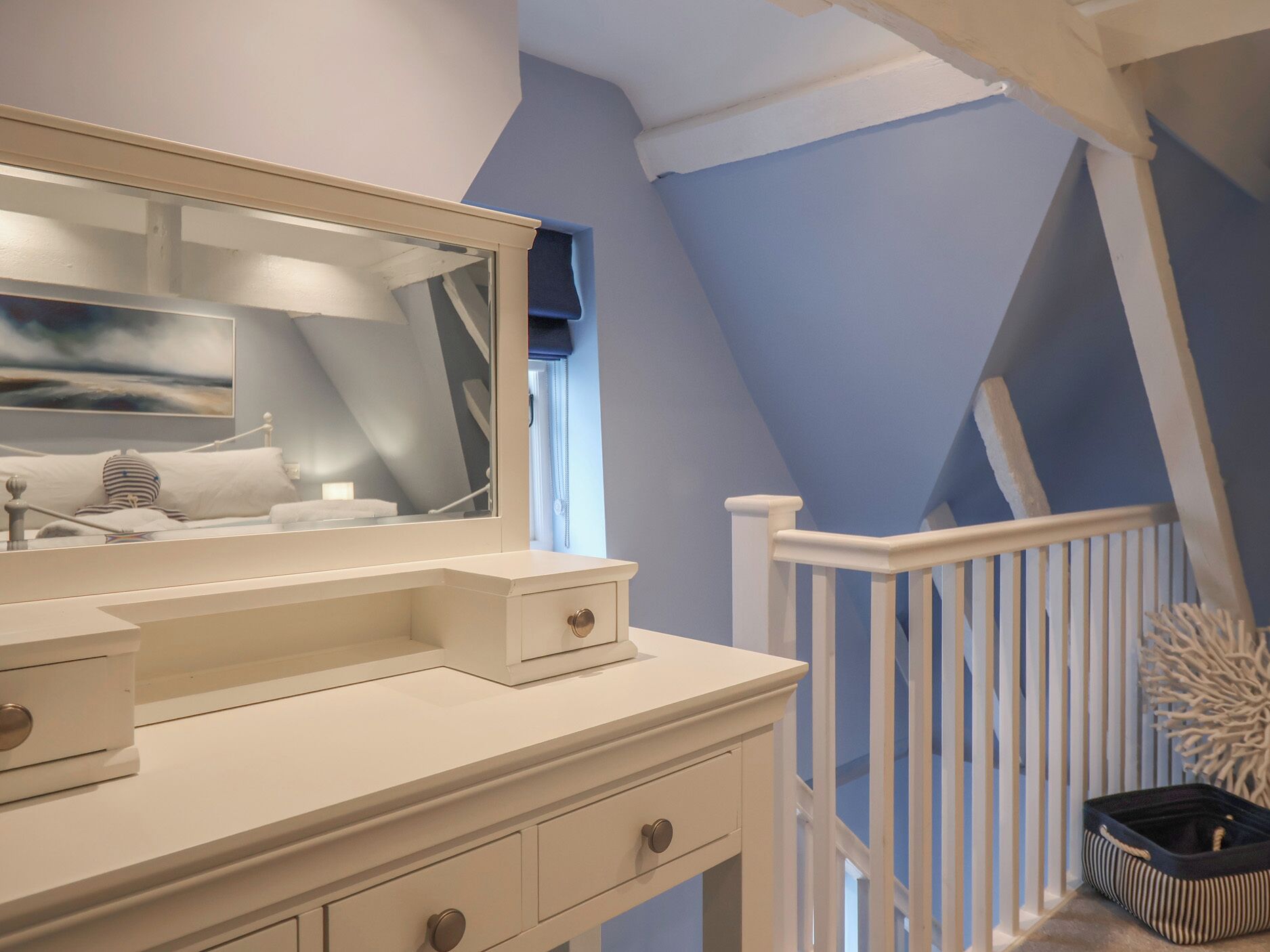 A bedroom with a white vanity, a large mirror, and a view of a blue room through a window.