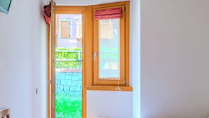 A bedroom with a bed, a window with a curtain, a door leading to a balcony, and a small table. - Raggio di Sole by Interhome (Carisolo)