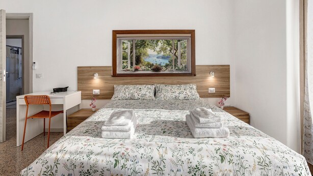 A bedroom with a bed, a desk, a chair, and a painting of a landscape. - B&B La Promessa – 'Amore' Room with Balcony, Wi-Fi, and Air Conditioning (Pregnana Milanese)
