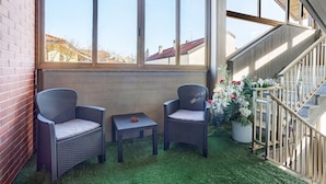 Een balkon met twee rieten stoelen, een tafeltje en een potplant.