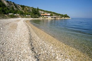 A pebble beach with clear water, a house with a red roof, and a hillside with trees. - Two-story Holiday Home for in Valica (Umag)