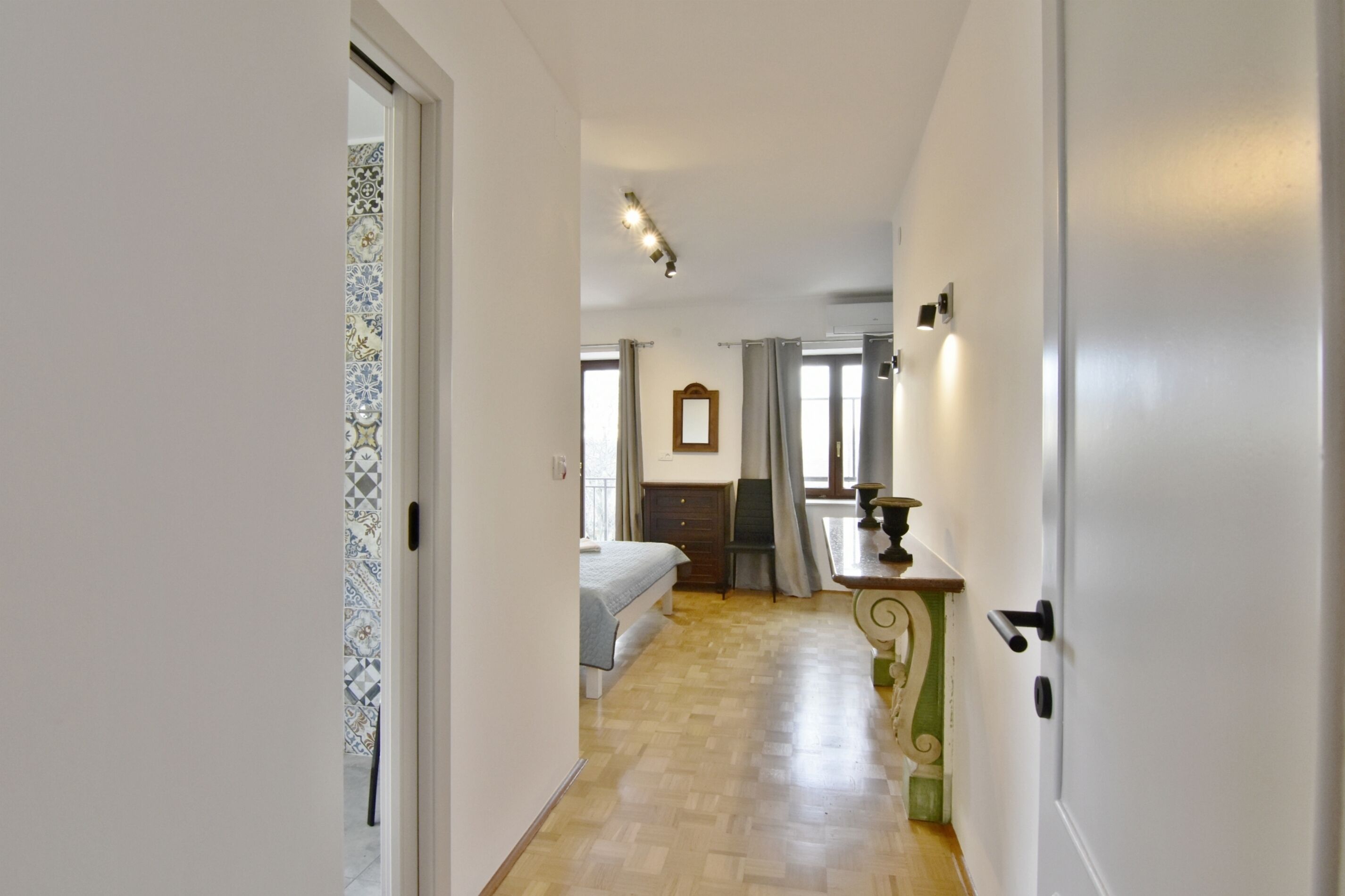Passadís estret amb un llit, una cambrera i un mirall en una habitació.