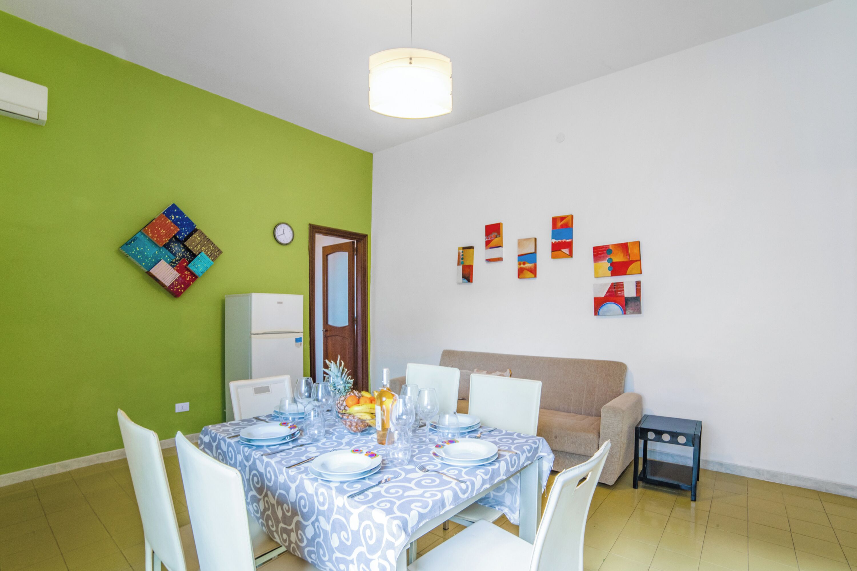 Un comedor con una mesa dispuesta para cuatro personas, un refrigerador y un sofá.