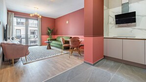 En moderne stue med sofa, spisebord, stole, et køkken med skabe og et stort vindue med gardiner.