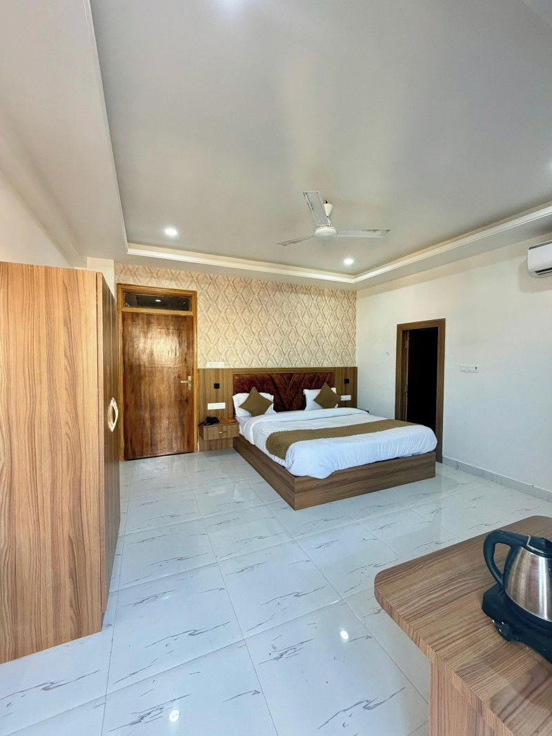 A hotel room with a bed, a wooden wardrobe, a desk with a kettle, and a ceiling fan.