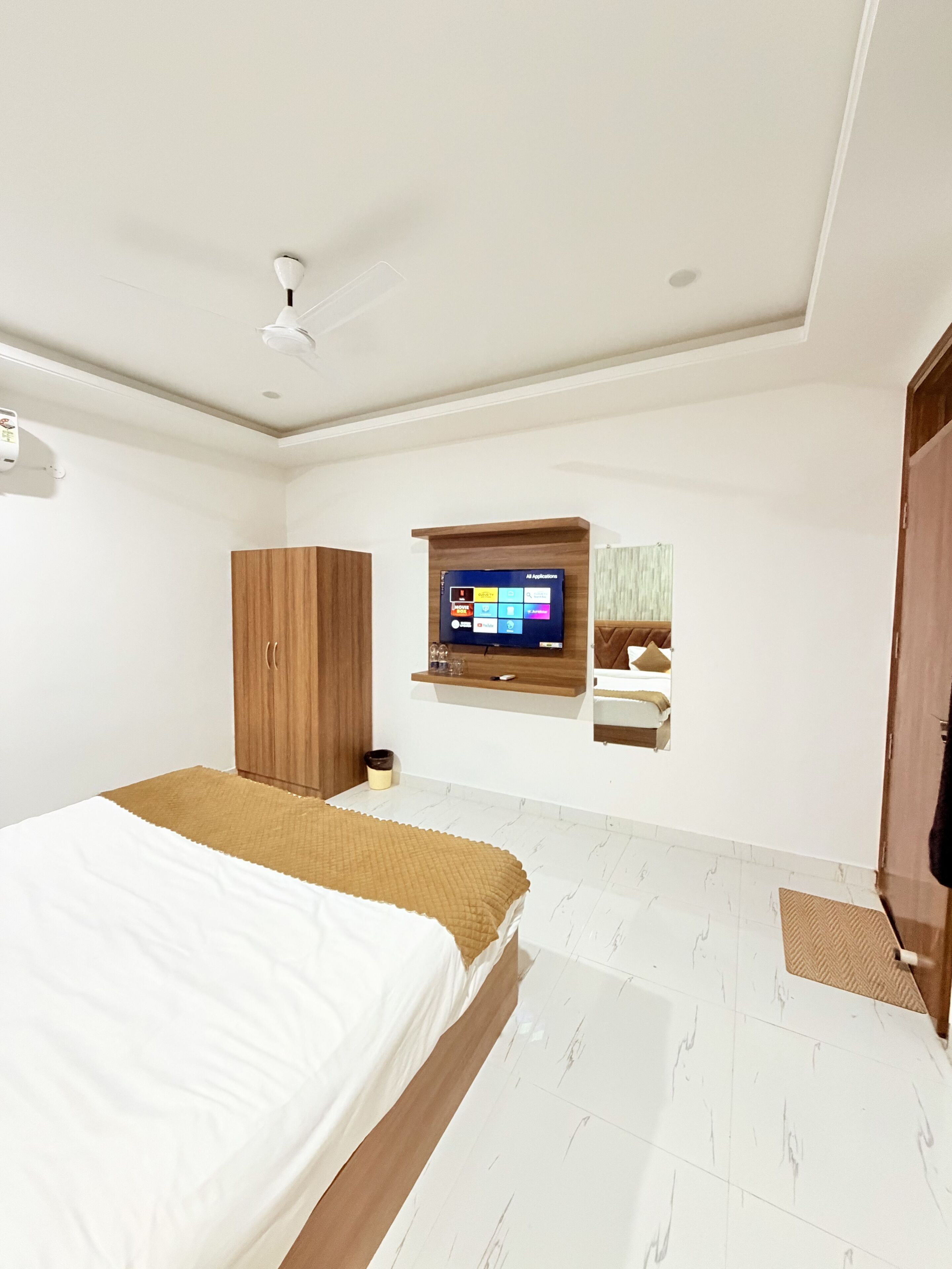 Ein Schlafzimmer mit einem Bett, einem Holzschrank, einem an der Wand befestigten Fernseher und einem kleinen Regal mit Gegenständen.