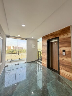 A modern interior with a polished marble floor, a wooden accent wall, and a view of buildings through a large window. - Shri Prem Sharnam -By The Aureo Hotels (Vrindavan)