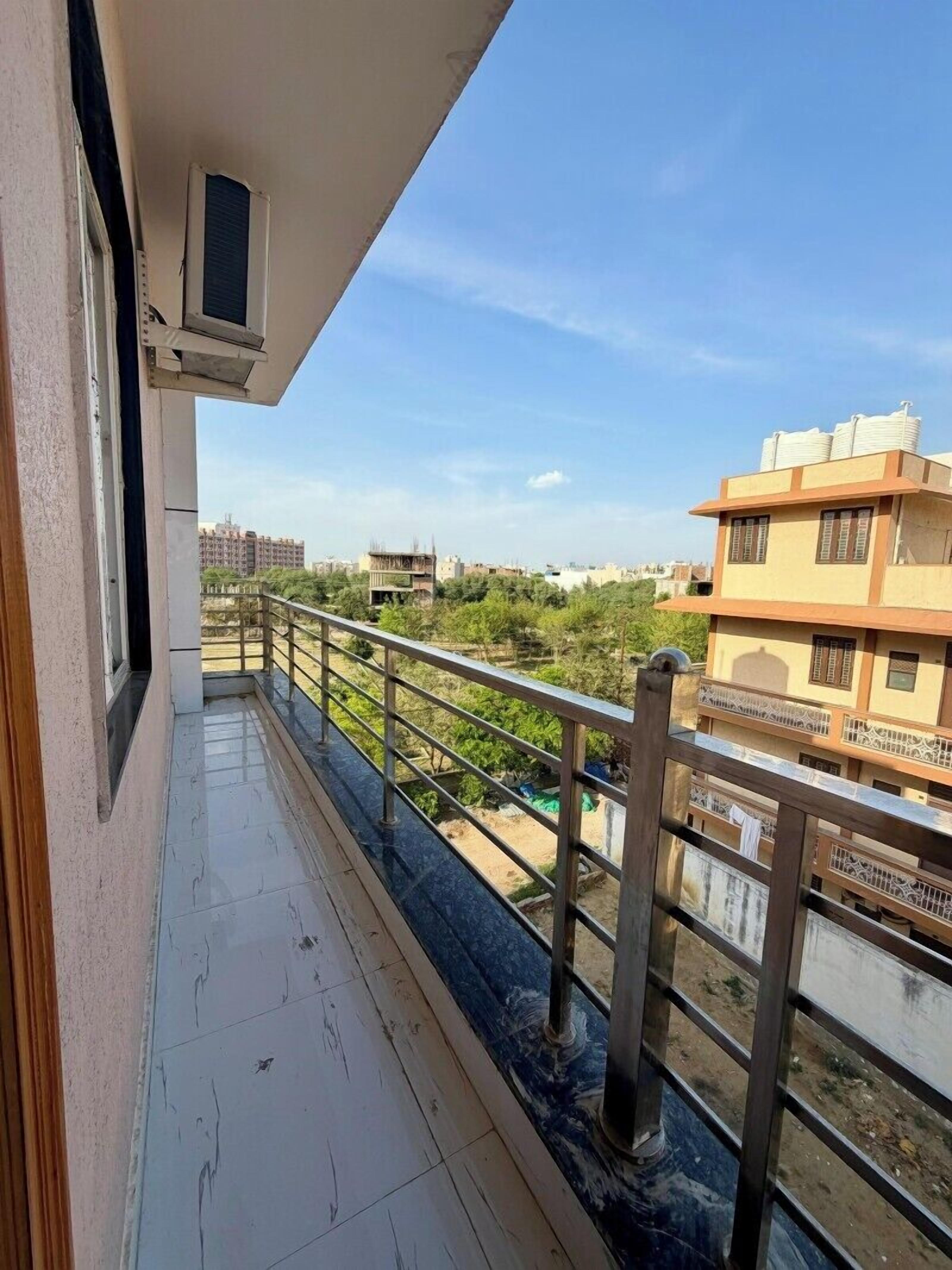 A balcony with a metal railing, a window with an air conditioning unit, and a view of a river and buildings in the distance.