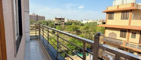 A balcony with a metal railing, a window with an air conditioning unit, and a view of a river and buildings in the distance.