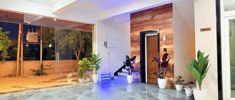 A modern hotel lobby with a marble floor, potted plants, and a wooden reception desk.