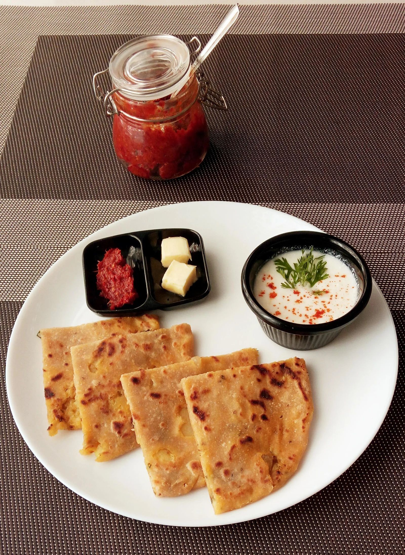 A plate with flatbreads, a small bowl of sauce, a jar of chutney, and a small dish of butter.