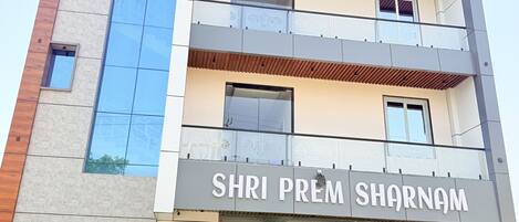 Um edifício de vários andares com uma placa na entrada que diz 'SHRI PREM SHARNAM'.