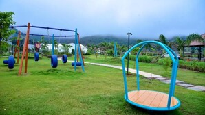 A playground with swings and tire swings, surrounded by grass and palm trees. - Double Room #7 (Igatpuri)