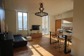 A modern living room with a sofa, a TV, and a dining area with stools.