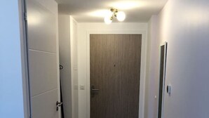 A narrow hallway with a wooden door at the end, white walls, and a light fixture above. - Appartement 48m² 1 chambre, garage, proche du lac (Aix-les-Bains)