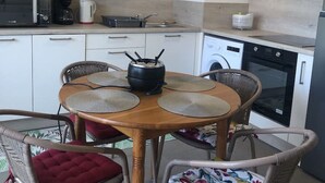 A compact kitchen with white cabinets, a microwave, a coffee maker, and a stove. There is a dining table with chairs and a small rug. - Appartement 48m² 1 chambre, garage, proche du lac (Aix-les-Bains)
