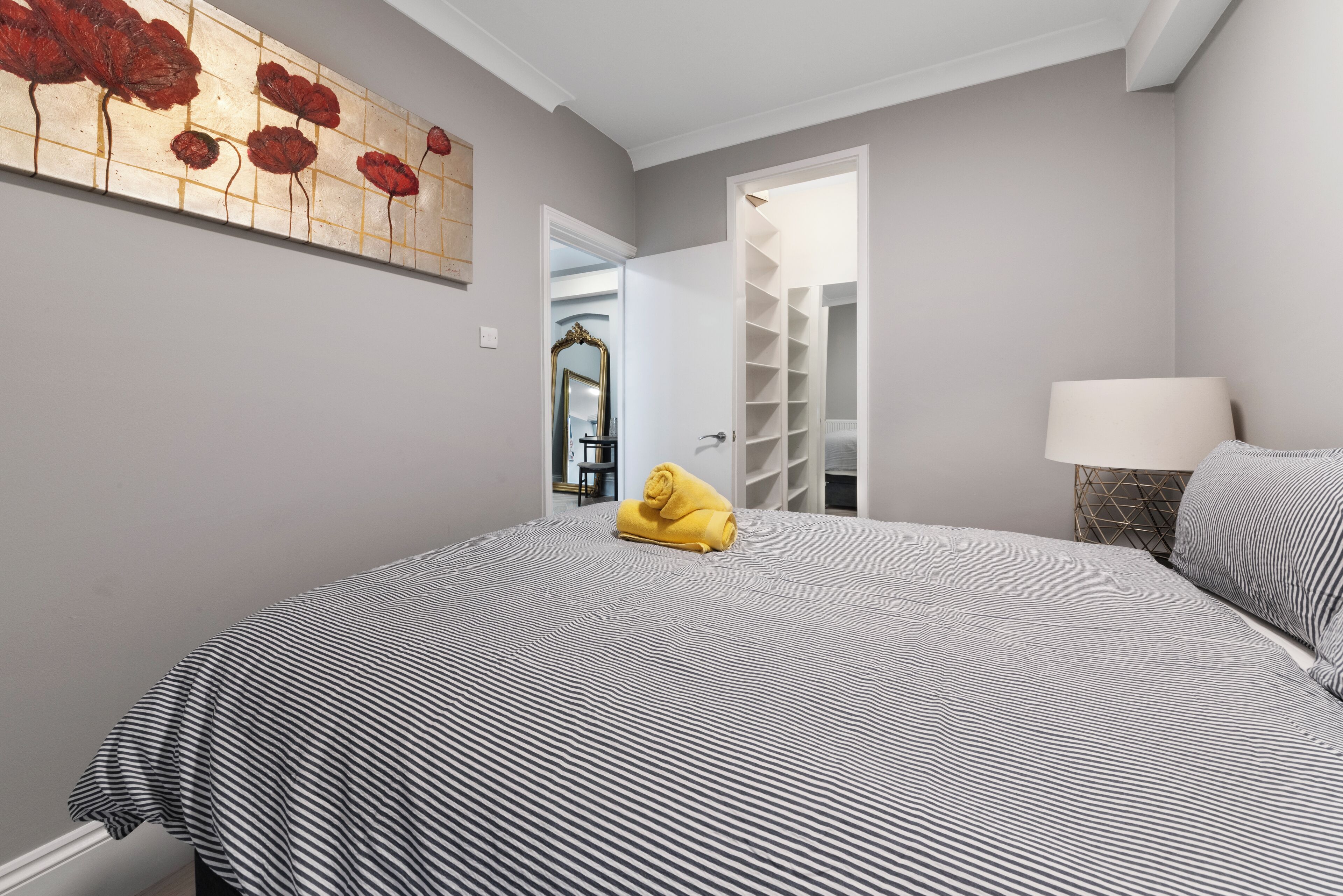 Una camera da letto con copriletto a righe, un asciugamano giallo, una lampada da comodino e uno specchio a parete.