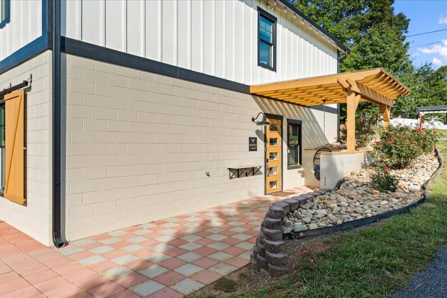 A modern building with a white exterior, a wooden pergola, a tiled entrance, and a stone pathway.