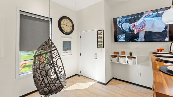 A modern room with a hanging chair, a clock, a television, and a view of a park.