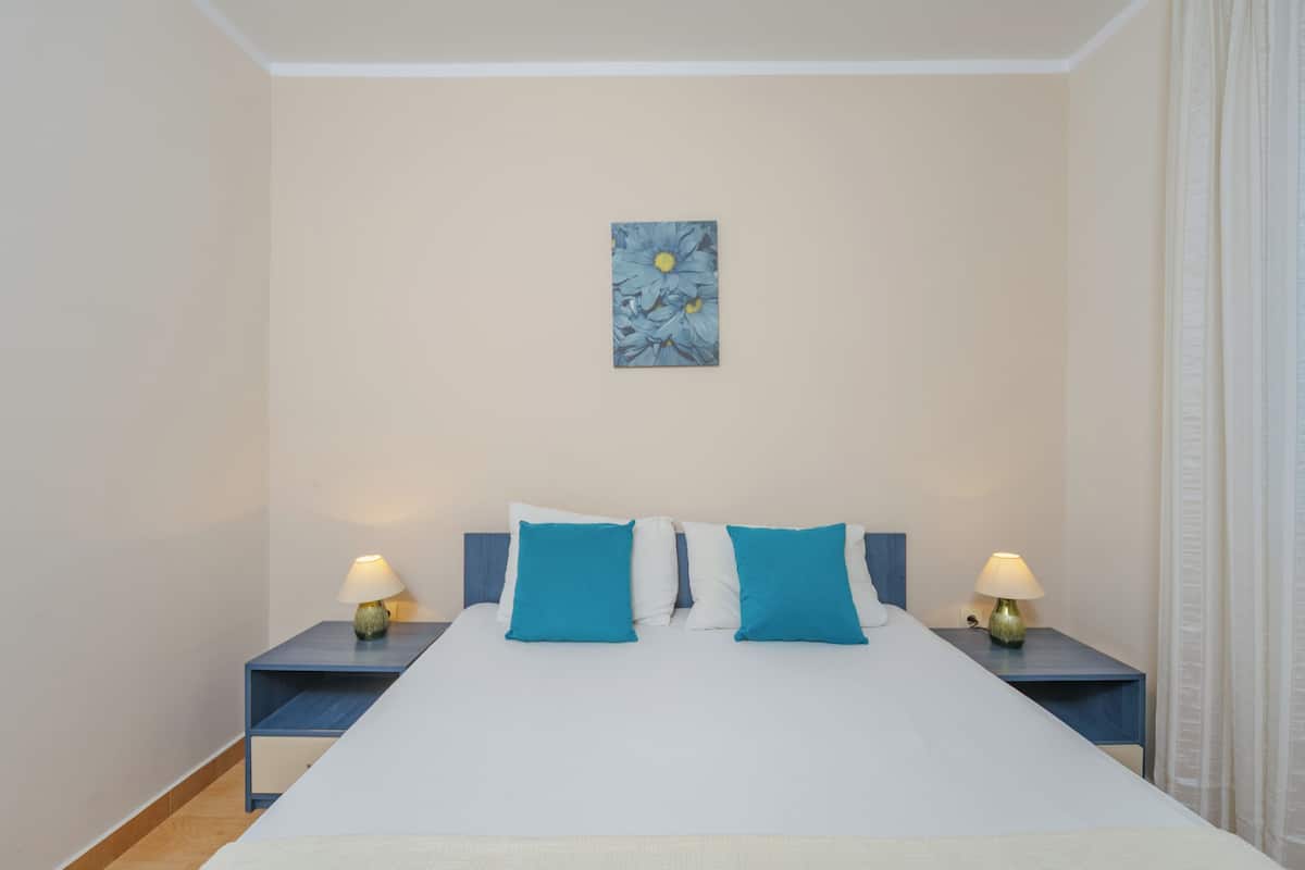 Een keurig ingerichte hotelkamer met een groot bed, twee nachtkastjes met lampen en een aan de muur hangend kunstwerk.