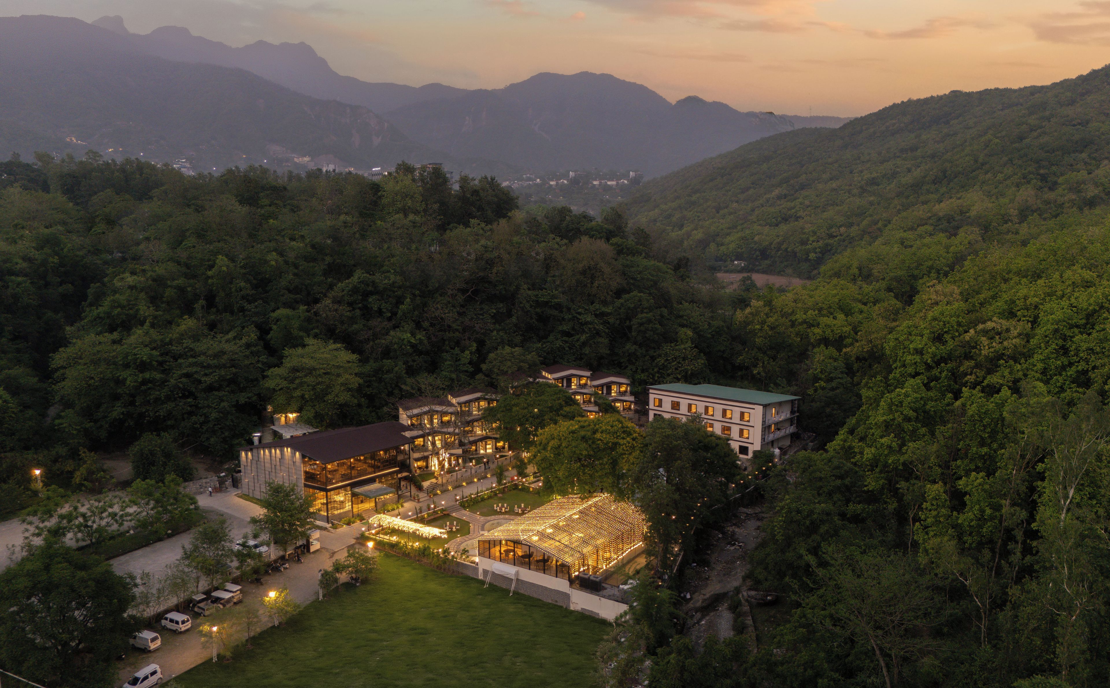 Ein großes, mehrgeschossiges Hotel mit Glasfassade, umgeben von üppiger Vegetation und Bergen im Hintergrund.