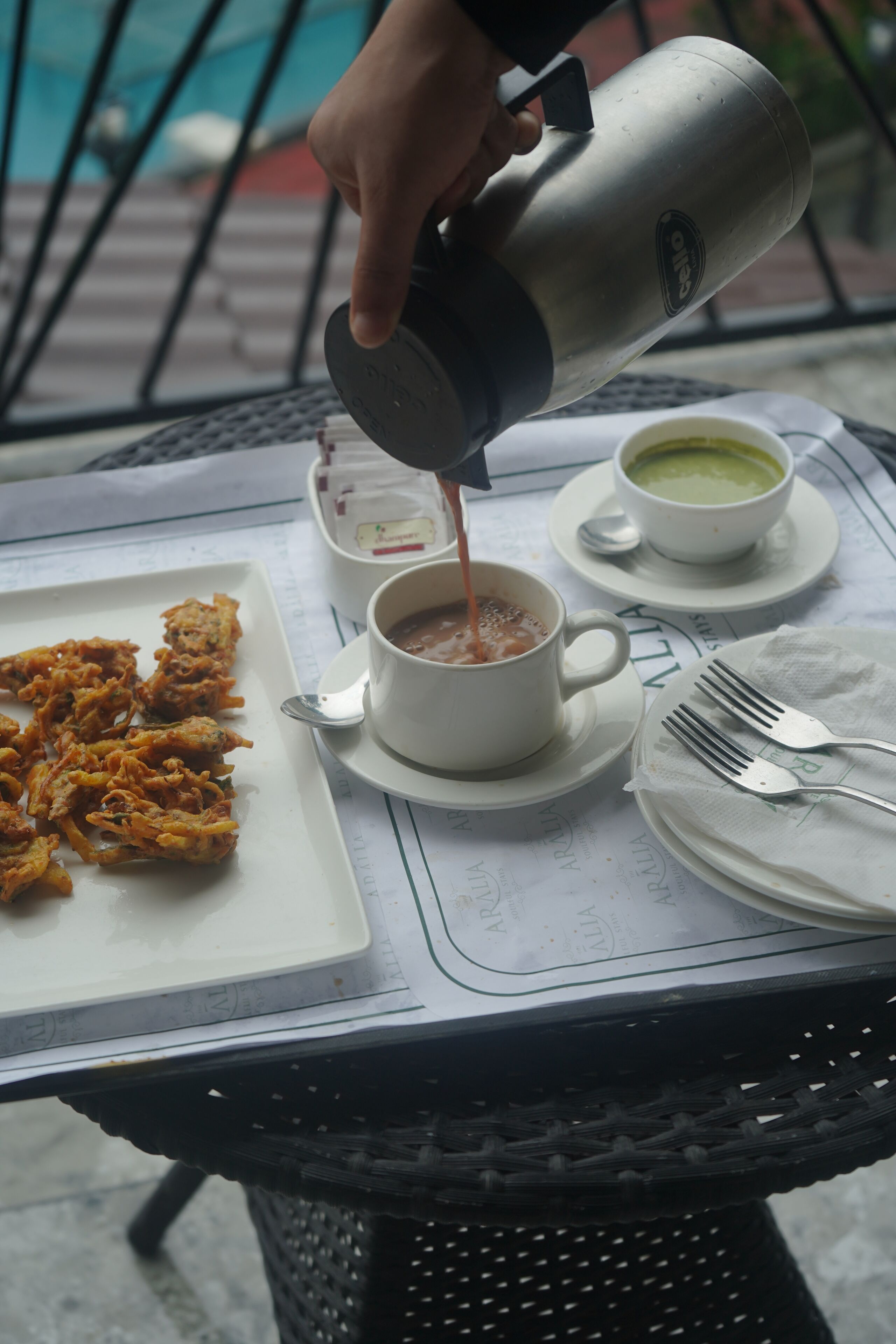 A table with a white plate of fried food, a cup of coffee, and a cup of green tea.