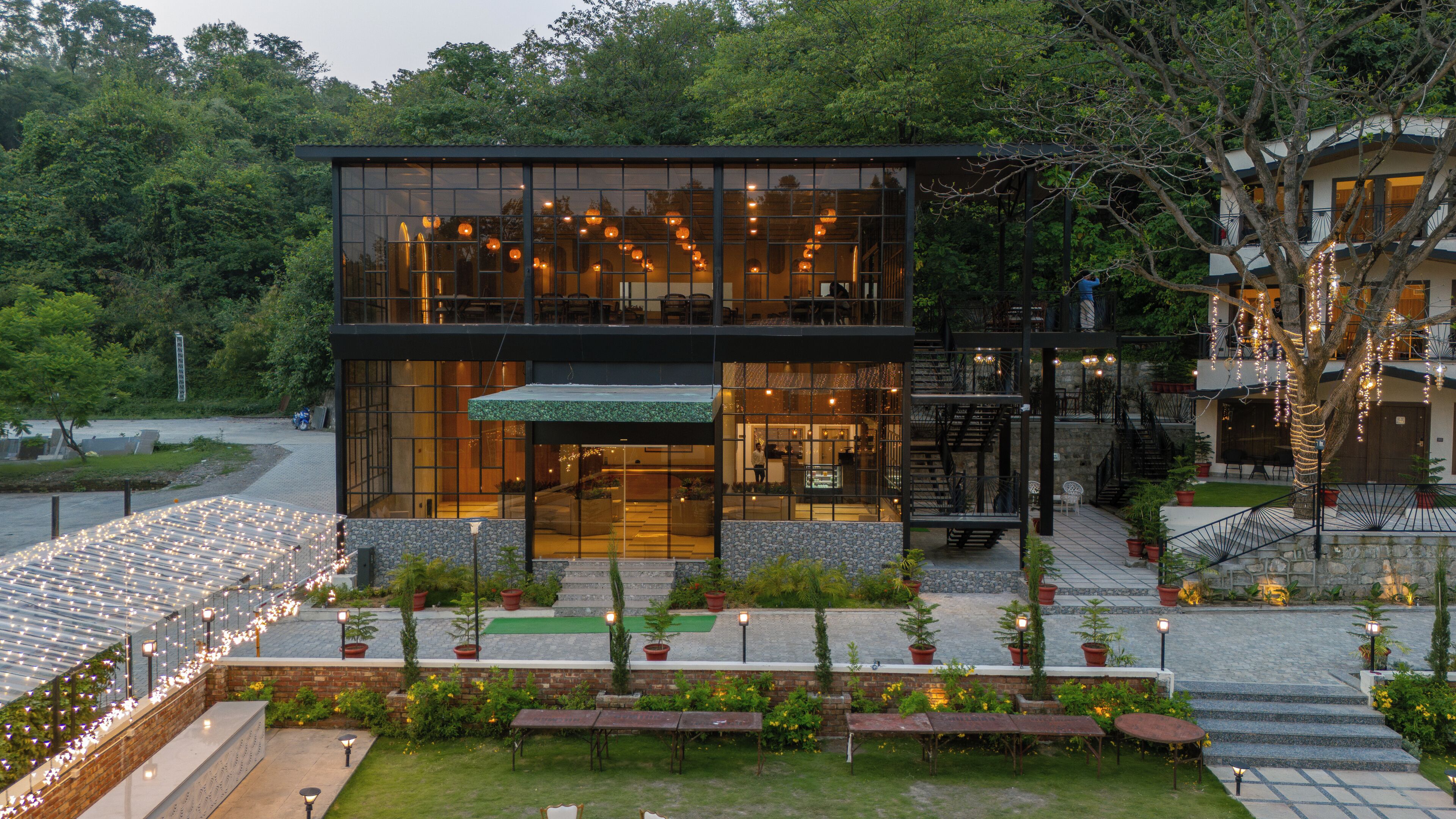 A modern building with a glass facade, outdoor seating, and a staircase leading to a second level.