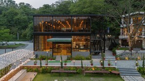A modern building with a glass facade, outdoor seating, and a staircase leading to a second level. - The Aralia (Dehradun)