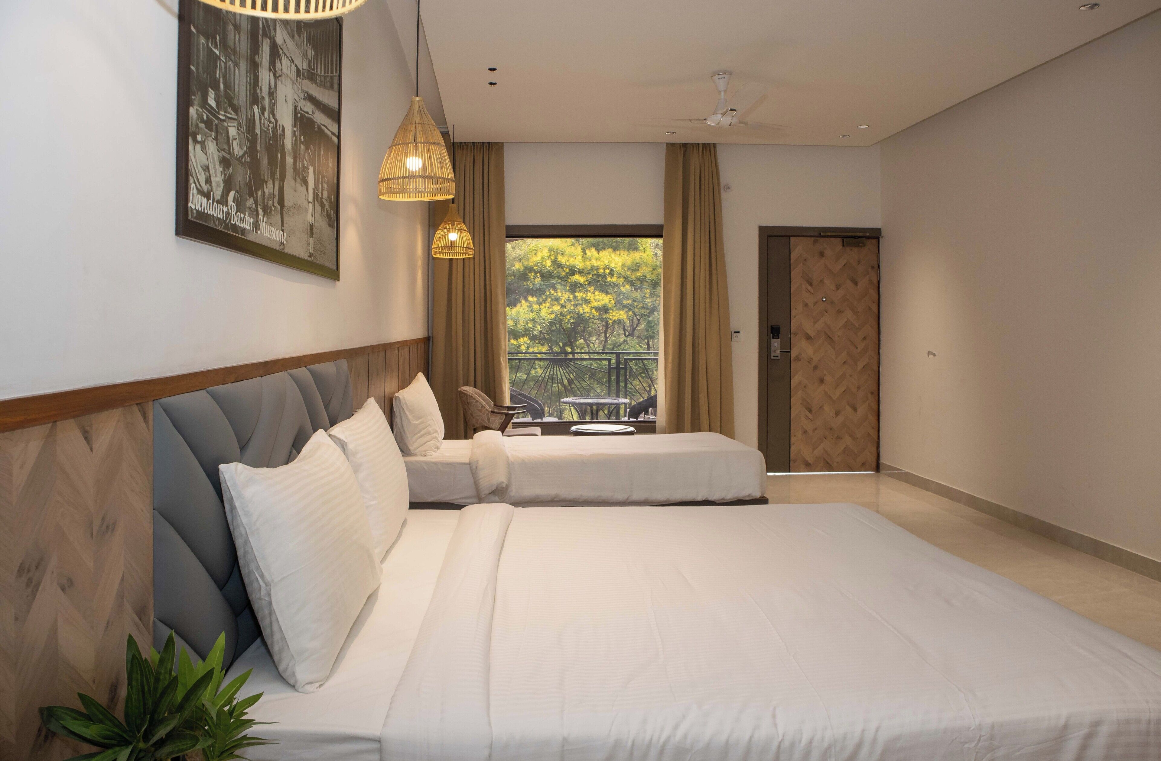A modern bedroom with a large bed, a view of the outdoors through a window, and a door leading to another room.