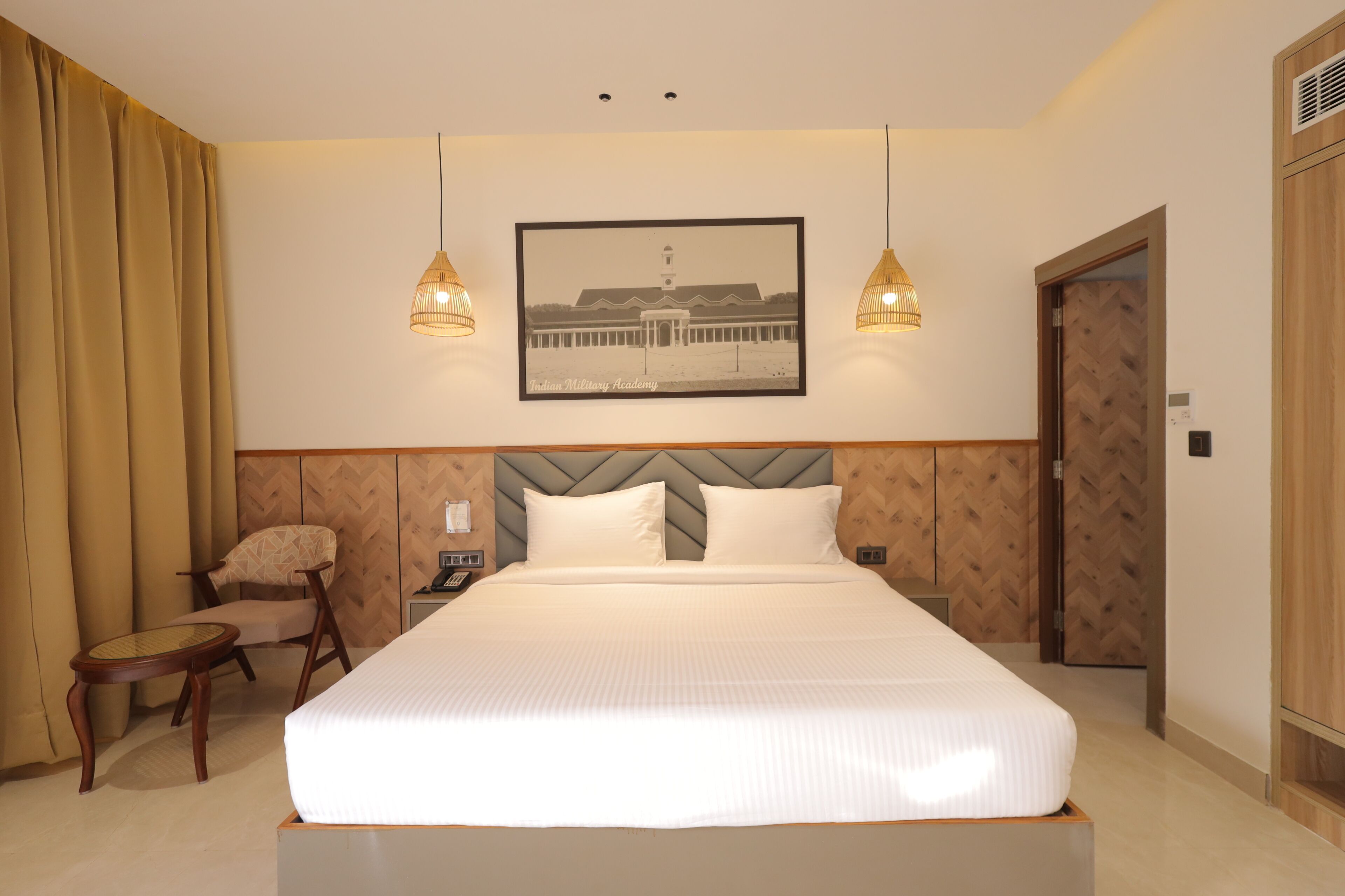 A hotel room with a large bed, two bedside lamps, a chair, a wooden headboard, and a framed picture on the wall.