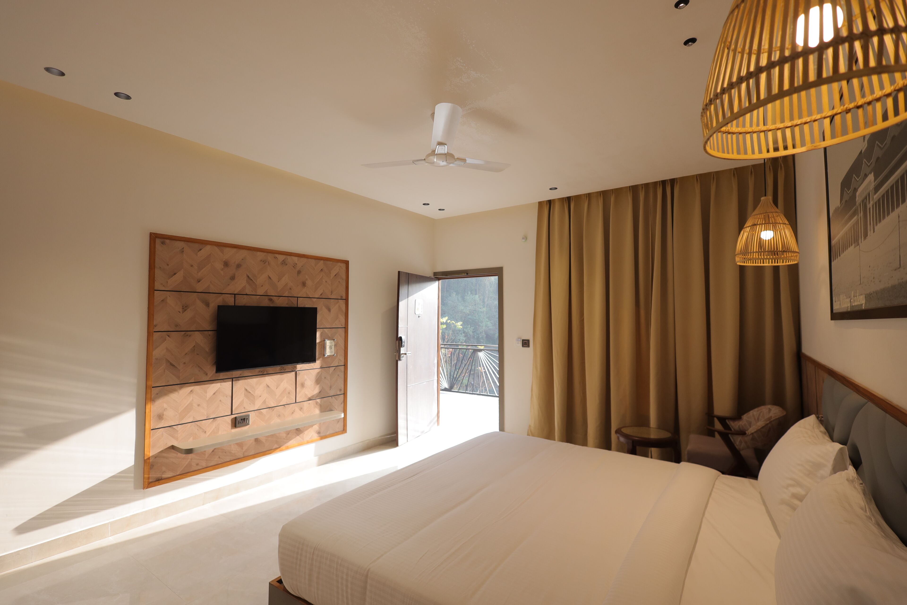 Ein Hotelzimmer mit einem großen Bett, einem an einer Holzvertäfelung montierten Fernseher, einem Deckenventilator, einem Balkon mit Aussicht und einer Pendelleuchte.