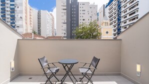A balcony with two chairs and a small table, overlooking a cityscape with tall buildings. - Complete Studios in Downtown Floripa - CMA (Florianópolis)