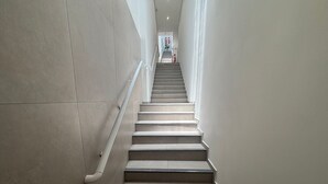 A staircase with a handrail, leading to a landing with a door and a plant. - Complete Studios in Downtown Floripa - CMA (Florianópolis)