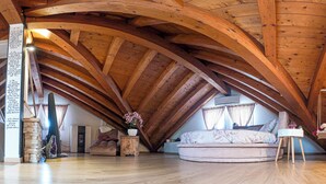 Ein geräumiges Dachzimmer mit Holzbalken, einer Steinwand, einer Couch und einem kleinen Tisch mit Blumen.