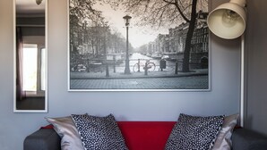 Ein Wohnzimmer mit einem roten Sofa, einem schwarz-weißen Stadtbildgemälde und einer weißen Stehlampe.