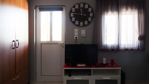 Ein Zimmer mit einem Holzschrank, einer Tür, einer Wanduhr, einem Fernseher auf einem Schrank und einem Fenster mit Vorhängen.